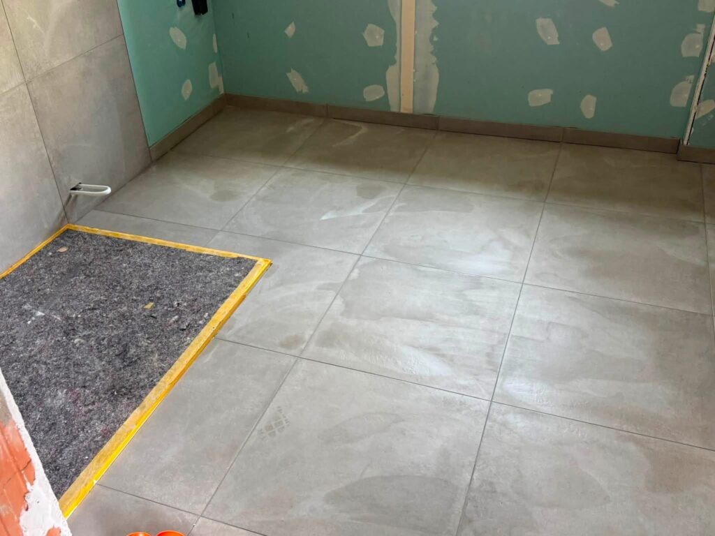 Großformatige Bodenfliesen im Badezimmer während der Sanierung, Duschbereich vorbereitet